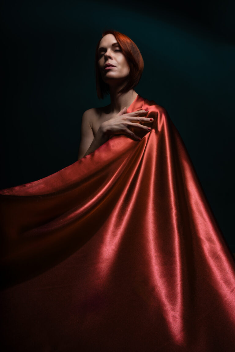 Das Bild einer Frau mit lebhaft roten Haaren, die ein ebenso rotes Tuch trägt. Die Frau wirkt selbstbewusst und strahlt eine kraftvolle Ausstrahlung aus.