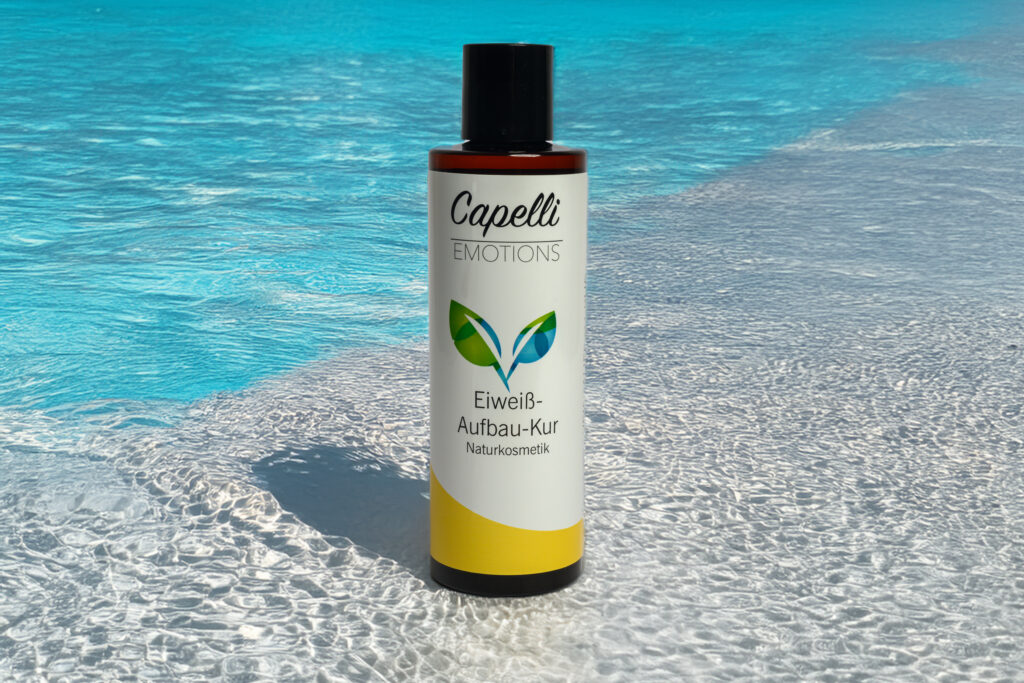 Produktfoto einer Flasche „Capelli Emotions Eiweiß-Aufbau-Kur Naturkosmetik“ stehend im klaren, sonnig beleuchteten Wasser mit türkisblauem Hintergrund. Professionelle Aufnahme für Produktfotografie.
