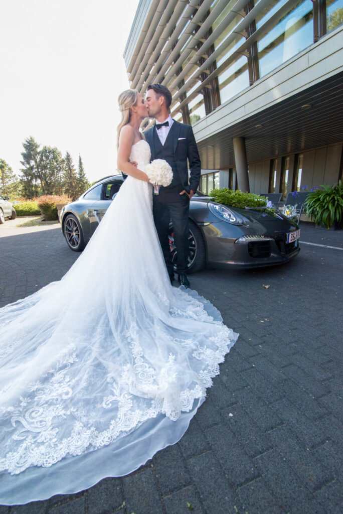 Romantisches Brautpaar mit langem Spitzenkleid vor einem Sportwagen – moderne Hochzeitsfotograf Goslar, Fotoagentur Otto