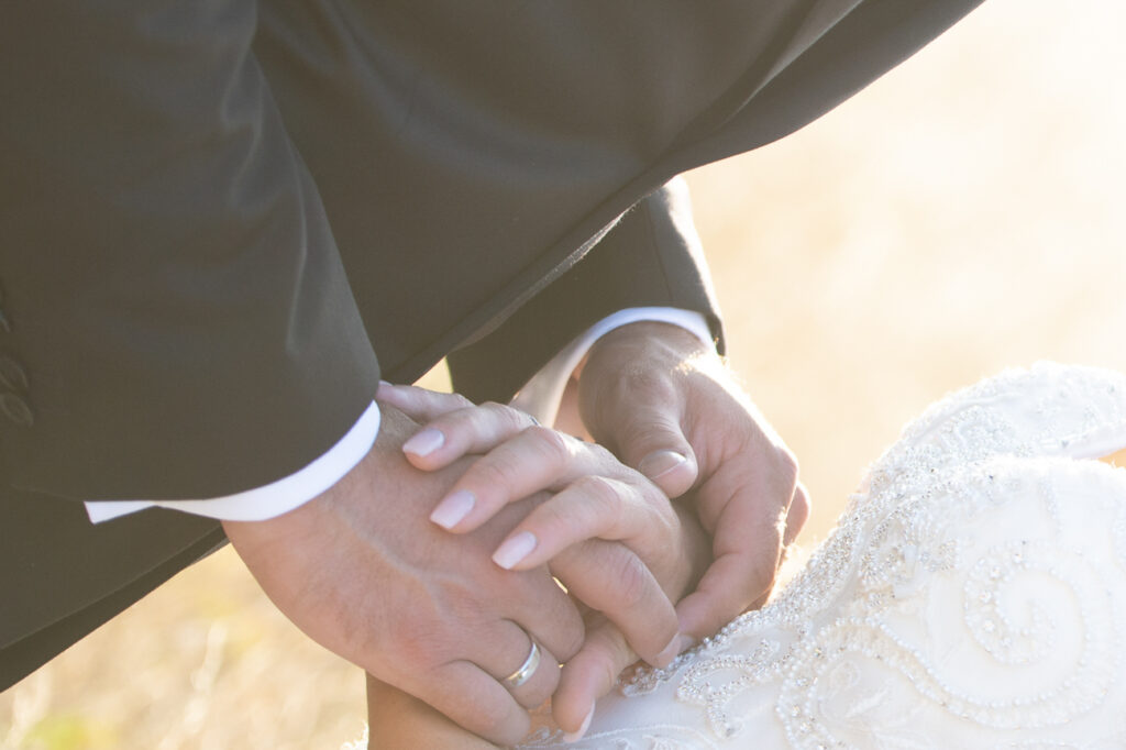 Detailaufnahme von ineinanderliegenden Händen eines Hochzeitspaares, mit Ehering und elegant besticktem Brautkleid im warmen Sonnenlicht – Hochzeitsfotografie, Fotograf Goslar, Fotoagentur Otto