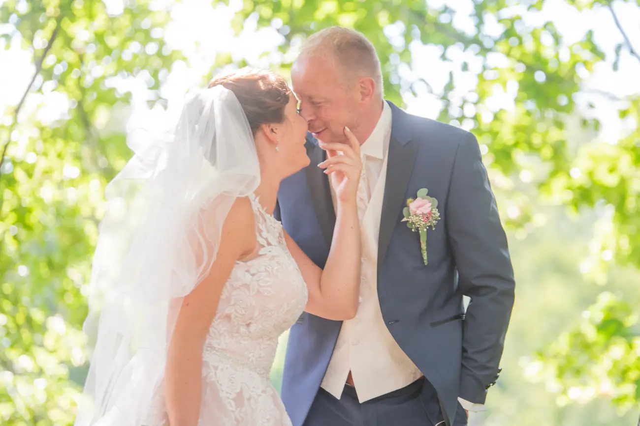 „Frühlingshaftes Hochzeitsfoto: Brautpaar küsst sich unter einem blühenden Baum, zarte Farben und natürliches Licht. Romantische Hochzeitsfotografie im Grünen, Fotograf in Goslar.“
