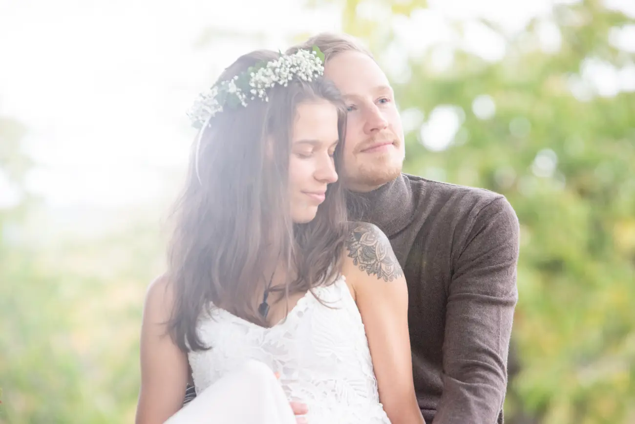 „Romantische Hochzeitsfotografie im Freien: Braut im weißen Kleid mit Blumenkranz lehnt sich an den Bräutigam, liebevolle Umarmung bei natürlichem Licht. Authentische Hochzeitsfotos von Fotograf in Goslar, Fotoagentur Otto.“