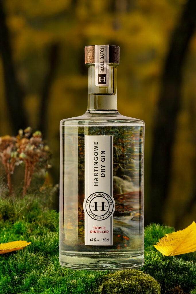 Produktfoto der Fotoagentur Otto aus Goslar – stilvolle Flasche „Hartingowe Dry Gin“ auf Moos mit herbstlicher Waldkulisse, klarer Gin mit edlem Etikett und Holzverschluss. Professionelle Produkt- und Getränkefotografie.